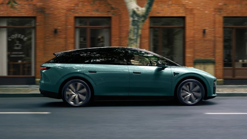 En sideprofil av 2026 Li i6, en blågrønn helelektrisk SUV, som kjører langs en bygate forbi en rødtegls bygning med en kaffebar og et tre.. Kilde: cnevpost.com